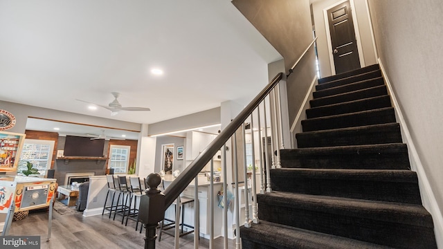 staircase with a fireplace, wood-type flooring, and ceiling fan