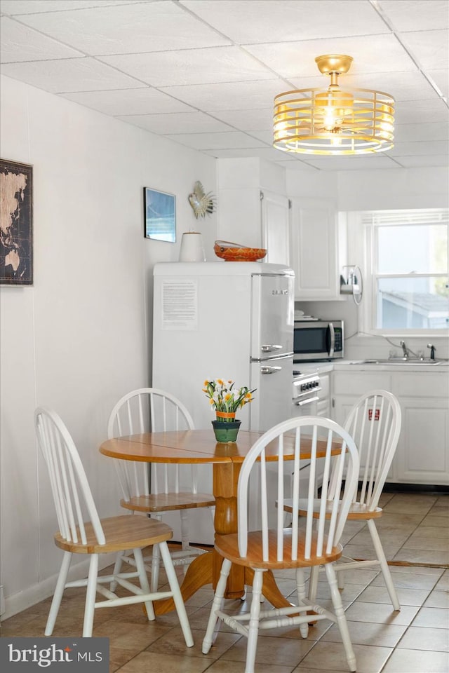 tiled dining space with sink, a paneled ceiling, and a notable chandelier