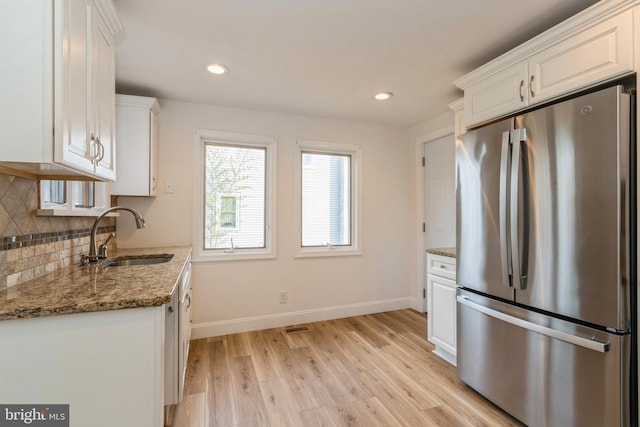 kitchen with sink, stainless steel fridge, stone countertops, white cabinets, and light wood-type flooring