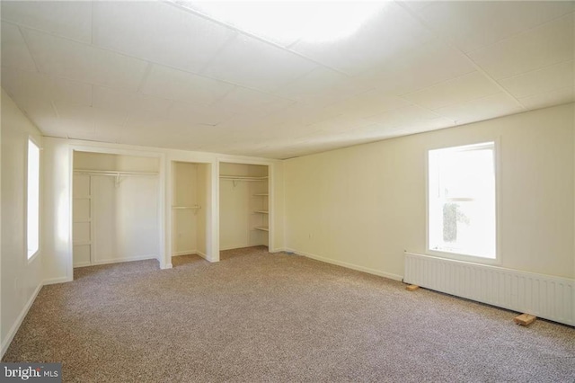 unfurnished bedroom with carpet flooring, radiator heating unit, and two closets