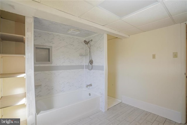 bathroom with a paneled ceiling, hardwood / wood-style flooring, and washtub / shower combination