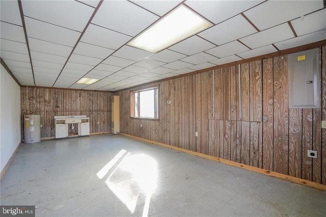 basement with electric panel, water heater, wooden walls, and a drop ceiling