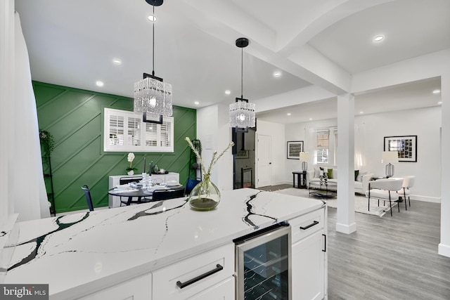 kitchen with light stone countertops, beverage cooler, decorative light fixtures, white cabinets, and light hardwood / wood-style floors