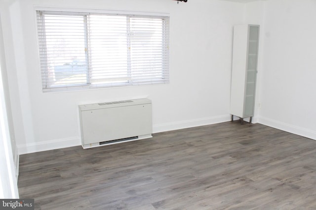 empty room with dark hardwood / wood-style flooring and heating unit