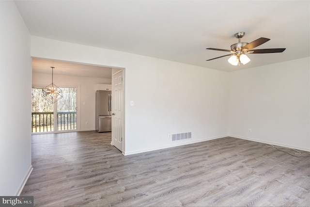 empty room featuring ceiling fan with notable chandelier and light hardwood / wood-style flooring