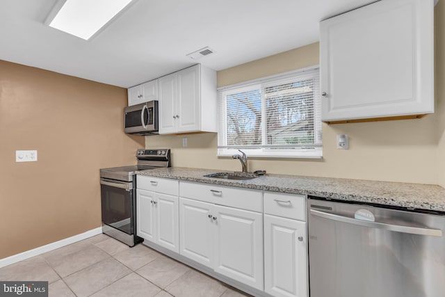 kitchen with light stone countertops, stainless steel appliances, sink, light tile patterned floors, and white cabinets