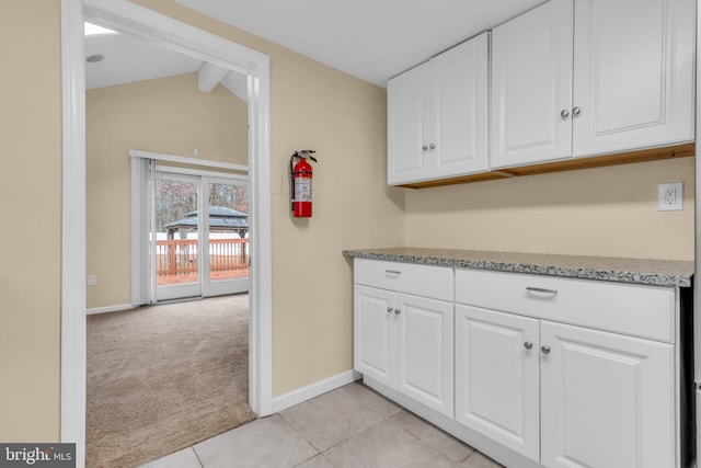 kitchen featuring vaulted ceiling with beams, light carpet, and white cabinets