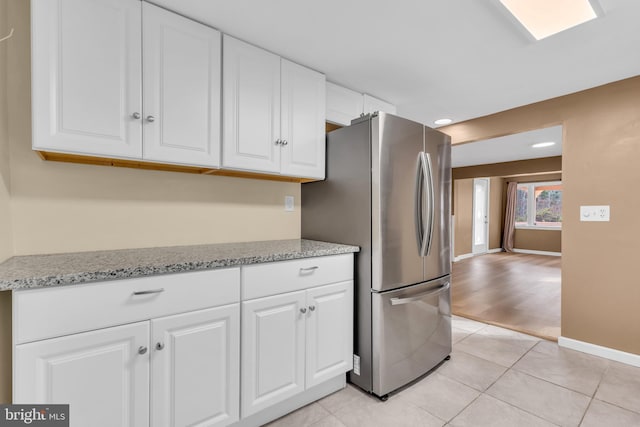 kitchen featuring light stone countertops, white cabinetry, stainless steel refrigerator, and light hardwood / wood-style flooring