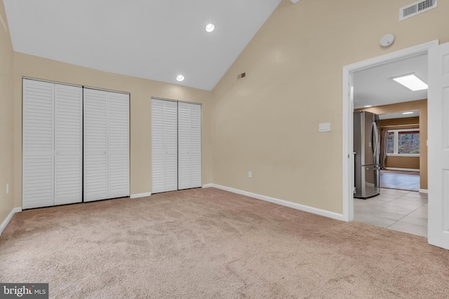 unfurnished bedroom with light carpet, stainless steel fridge, two closets, and high vaulted ceiling