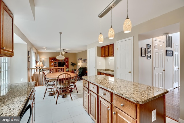 kitchen with ceiling fan, a center island, light stone counters, and hanging light fixtures