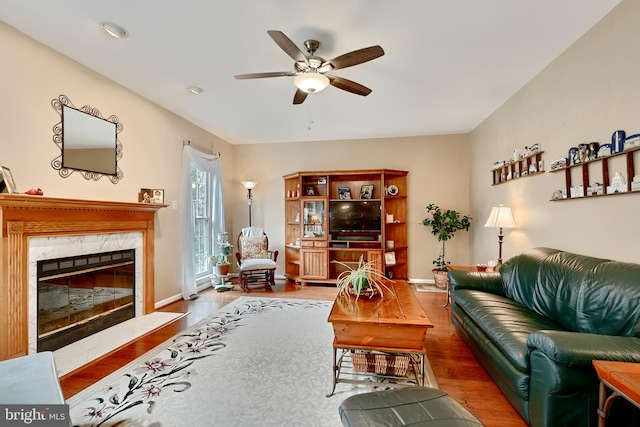 living room featuring a premium fireplace, ceiling fan, and wood-type flooring