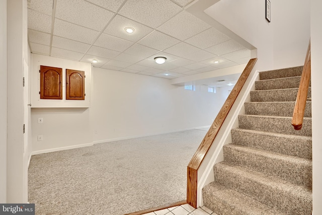 basement with a paneled ceiling and light colored carpet