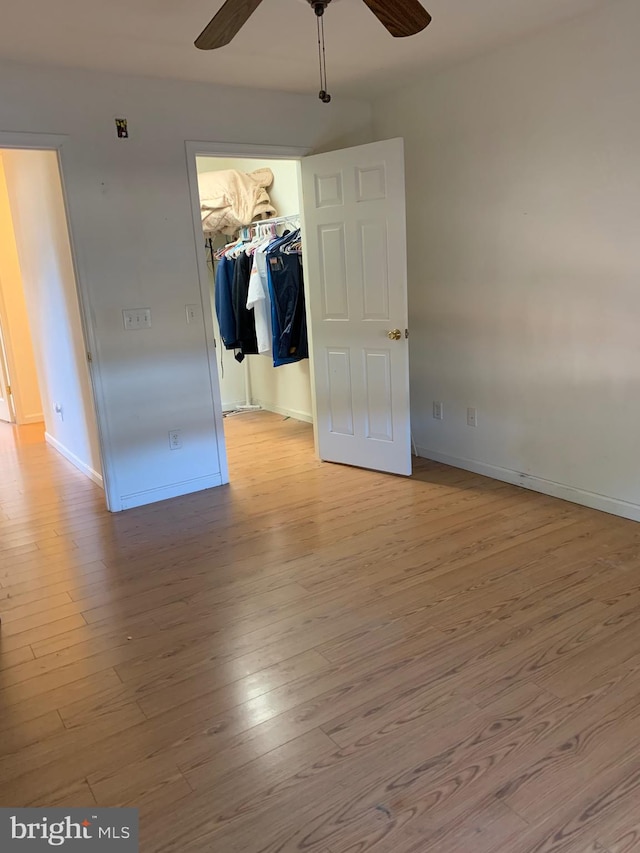 unfurnished bedroom with ceiling fan, a closet, a spacious closet, and light hardwood / wood-style flooring