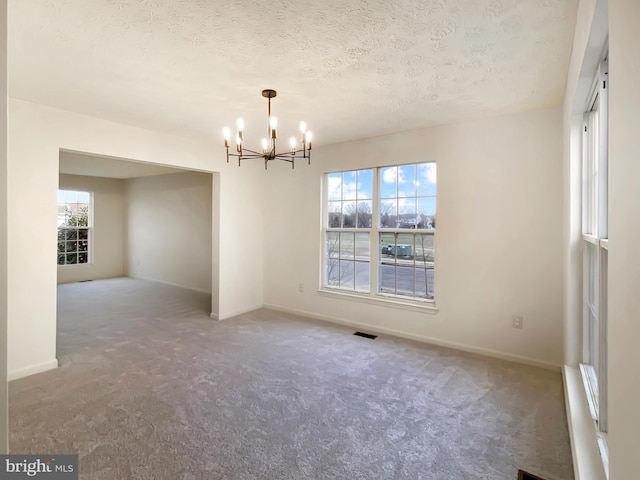 spare room featuring a notable chandelier, carpet floors, and a healthy amount of sunlight