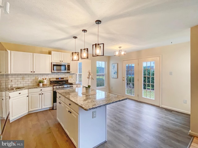 kitchen with appliances with stainless steel finishes, a kitchen island, pendant lighting, light stone countertops, and white cabinets