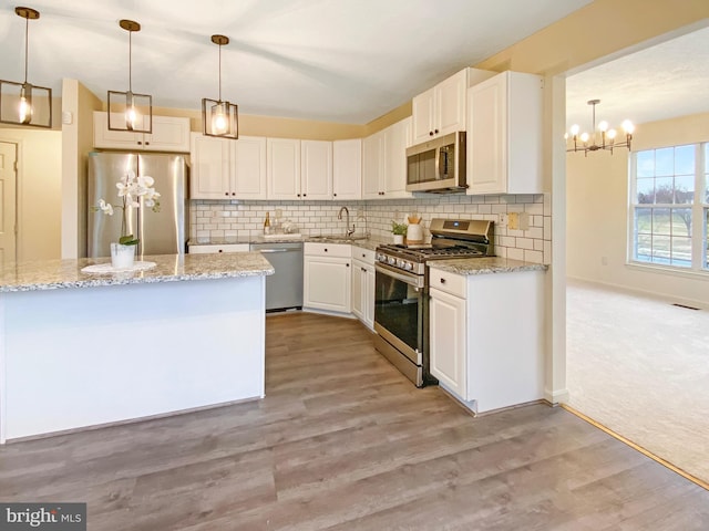 kitchen with hanging light fixtures, appliances with stainless steel finishes, white cabinets, and light stone counters