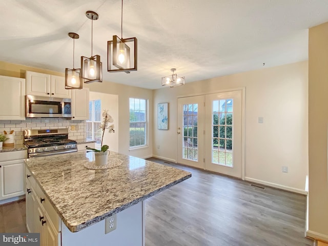 kitchen with a kitchen island, appliances with stainless steel finishes, pendant lighting, white cabinets, and backsplash