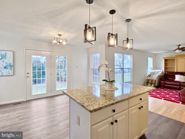 kitchen with hanging light fixtures, wood-type flooring, light stone countertops, and a center island