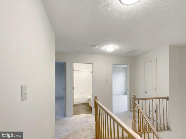 corridor with light carpet and a textured ceiling