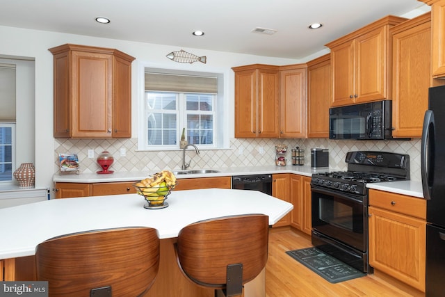 kitchen featuring decorative backsplash, a kitchen breakfast bar, sink, black appliances, and light hardwood / wood-style floors