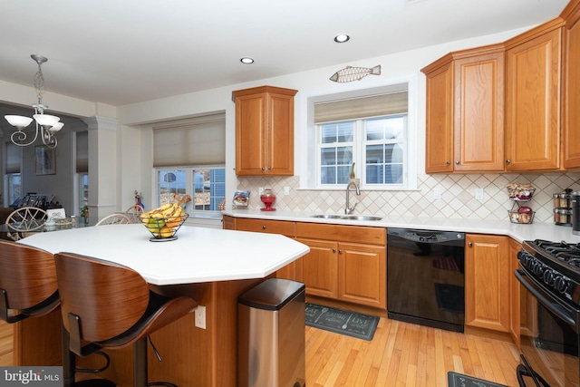 kitchen with decorative backsplash, light wood-type flooring, sink, black appliances, and hanging light fixtures