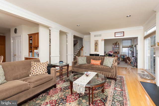 living room with light wood-type flooring, ornamental molding, and decorative columns