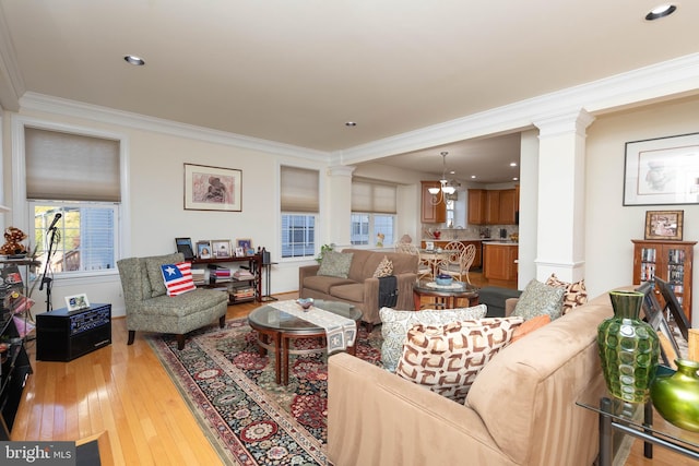 living room with decorative columns, an inviting chandelier, ornamental molding, and light wood-type flooring