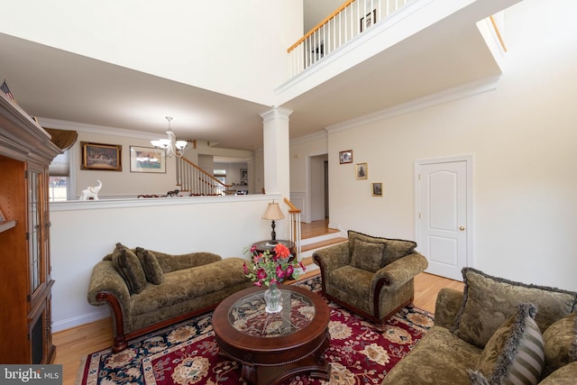 living room featuring an inviting chandelier, light wood-type flooring, crown molding, and decorative columns