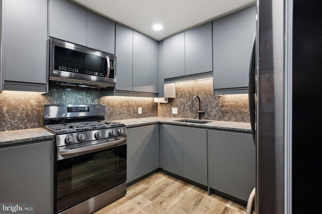 kitchen featuring stainless steel appliances, gray cabinetry, light wood-type flooring, dark stone countertops, and sink