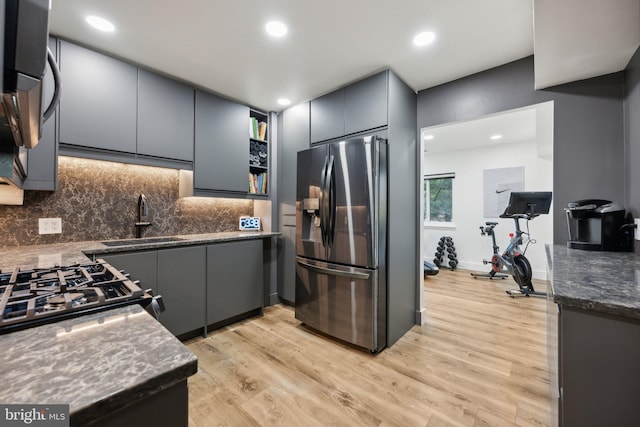 kitchen with gray cabinets, sink, light hardwood / wood-style flooring, stainless steel appliances, and dark stone counters