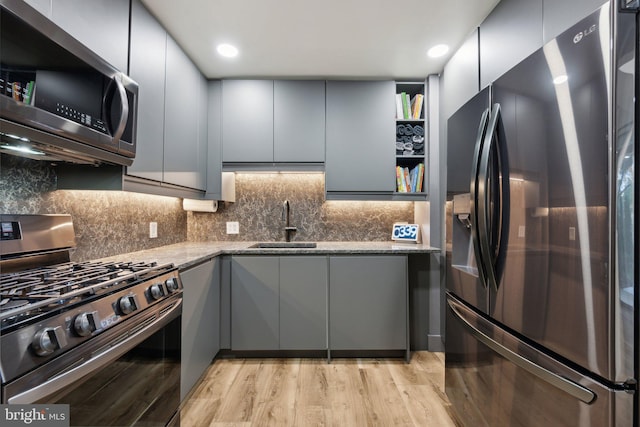 kitchen featuring light stone countertops, appliances with stainless steel finishes, sink, light wood-type flooring, and gray cabinetry