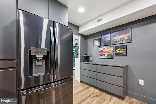 kitchen with light wood-type flooring, stainless steel fridge, gray cabinets, and stone countertops