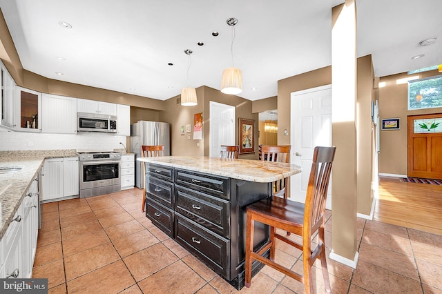 kitchen featuring a center island, white cabinets, hanging light fixtures, a kitchen bar, and stainless steel appliances