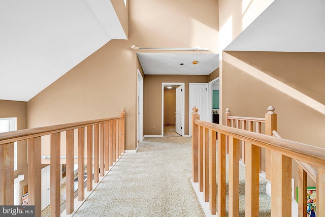 corridor featuring light colored carpet, vaulted ceiling, and a wealth of natural light