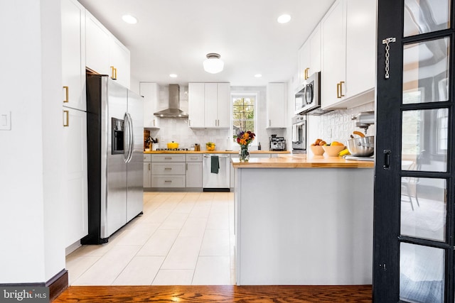 kitchen featuring wall chimney exhaust hood, wood counters, backsplash, white cabinets, and appliances with stainless steel finishes