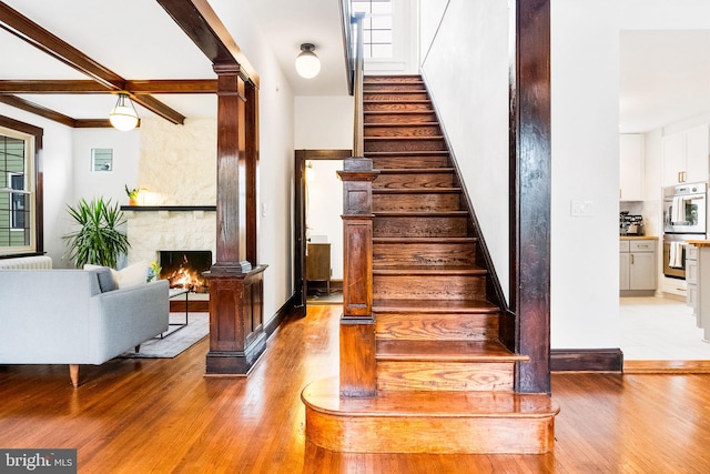 staircase featuring beamed ceiling, wood-type flooring, and a stone fireplace