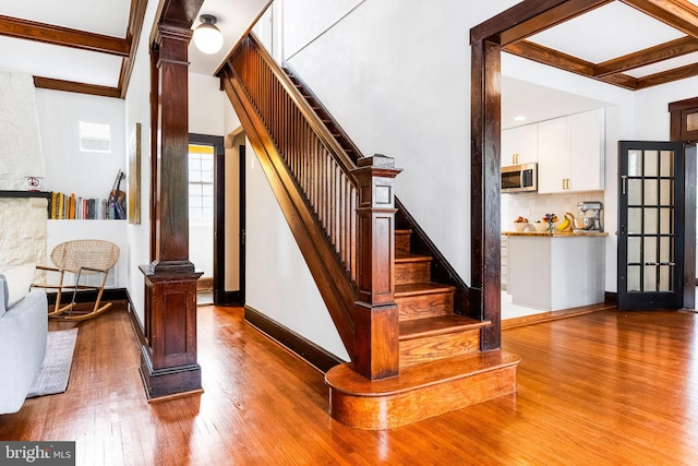 stairs with ornate columns, beamed ceiling, and wood-type flooring