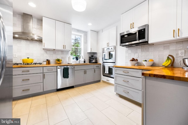 kitchen with white cabinetry, wooden counters, wall chimney range hood, and appliances with stainless steel finishes