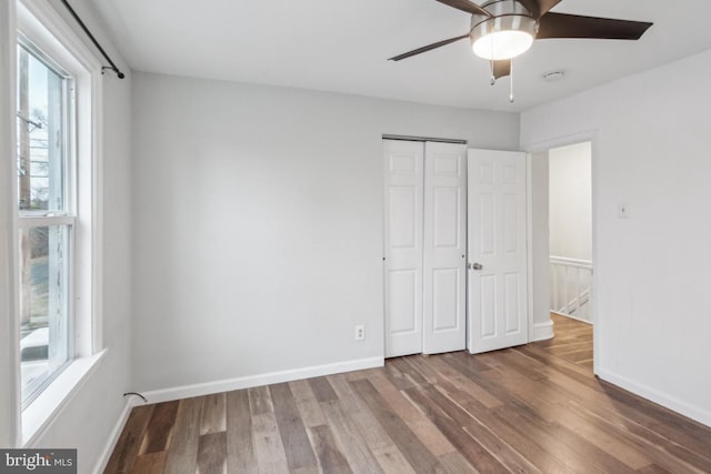 unfurnished bedroom featuring hardwood / wood-style floors, a closet, multiple windows, and ceiling fan