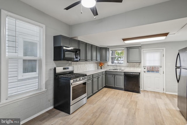 kitchen with black appliances, gray cabinetry, sink, and light hardwood / wood-style flooring