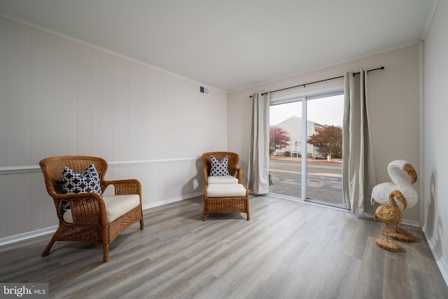 living area featuring light hardwood / wood-style floors, crown molding, and wood walls