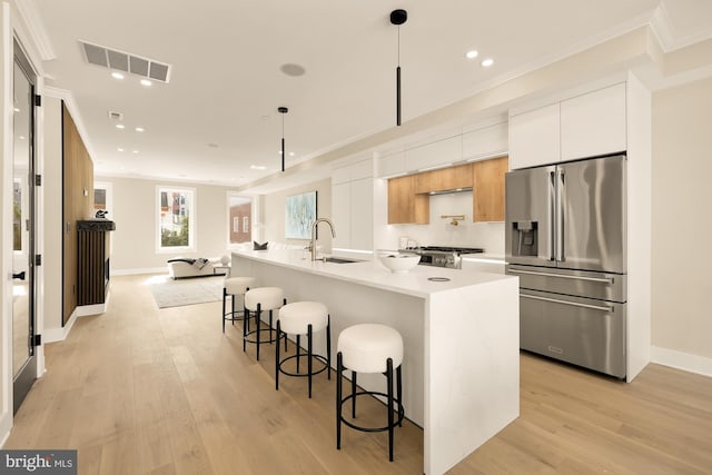 kitchen featuring high end fridge, sink, decorative light fixtures, white cabinets, and an island with sink