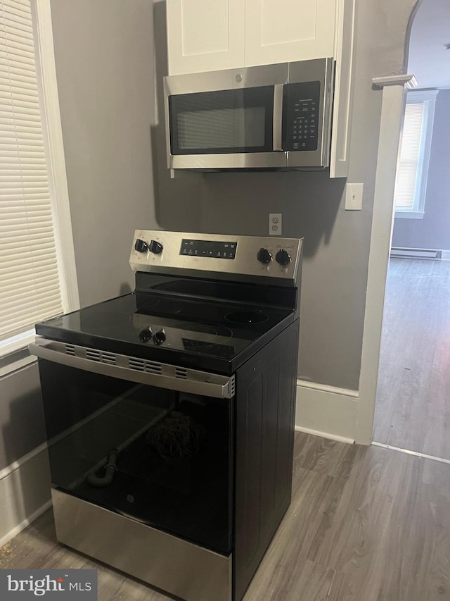 kitchen with white cabinets, appliances with stainless steel finishes, a baseboard heating unit, and hardwood / wood-style floors