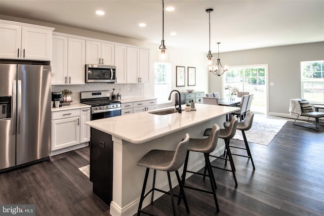 kitchen with dark wood-type flooring, hanging light fixtures, a center island with sink, white cabinets, and appliances with stainless steel finishes