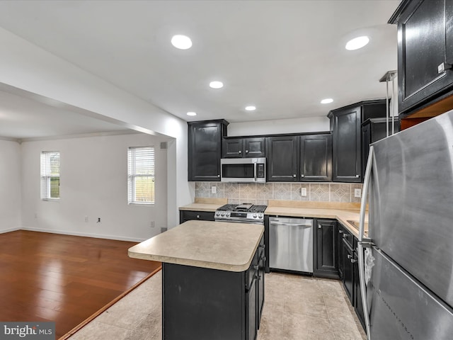 kitchen with tasteful backsplash, light hardwood / wood-style flooring, crown molding, a kitchen island, and appliances with stainless steel finishes