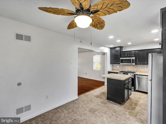 kitchen featuring ceiling fan, stainless steel appliances, backsplash, a kitchen island, and light wood-type flooring