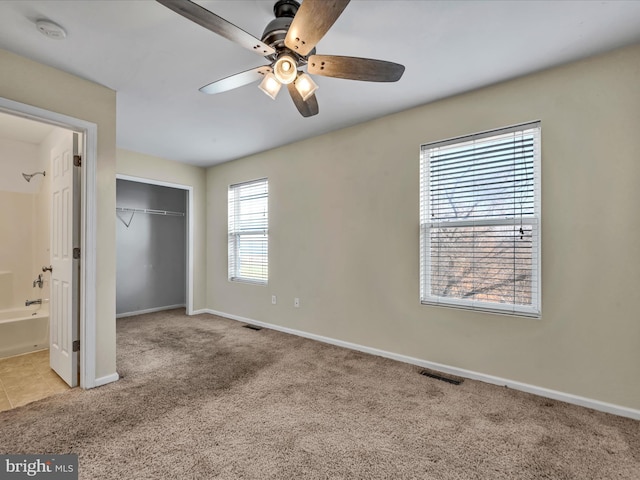 unfurnished bedroom featuring connected bathroom, light carpet, a closet, and ceiling fan