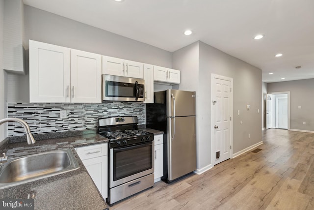 kitchen with appliances with stainless steel finishes, backsplash, sink, light hardwood / wood-style flooring, and white cabinets