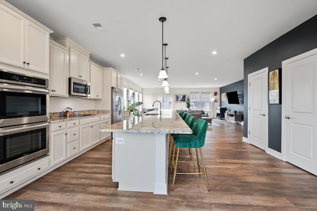 kitchen featuring decorative light fixtures, dark wood-type flooring, stainless steel appliances, and an island with sink