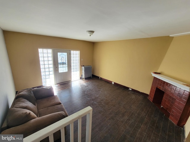 living room with radiator heating unit, dark hardwood / wood-style flooring, and a brick fireplace